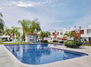 A swimming pool surrounded by modern buildings, palm trees, and a clear sky. - Riviera Nayarit Brand New House Close To The Beach (Bucerías)