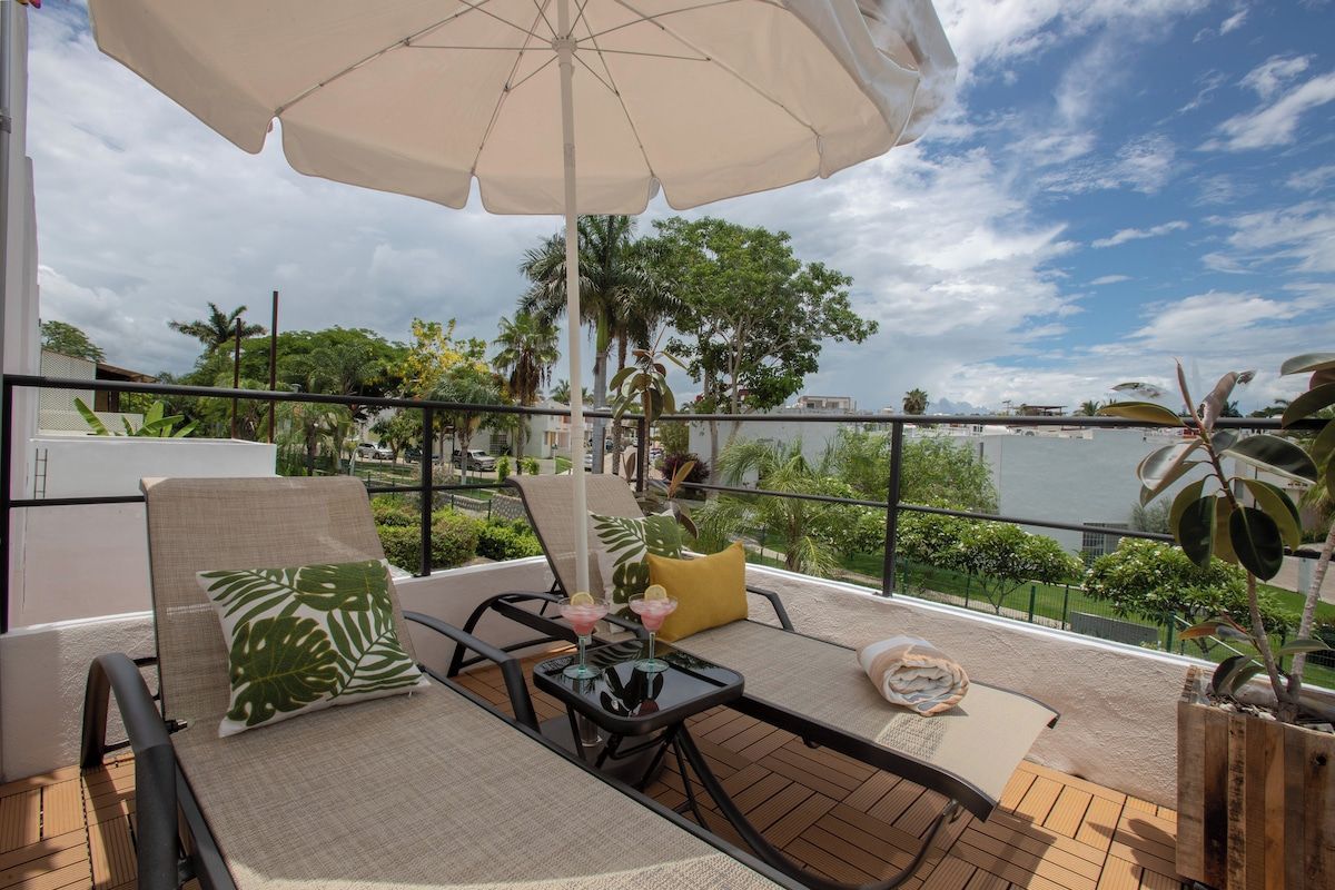 A balcony with lounge chairs, a table, and a large umbrella.