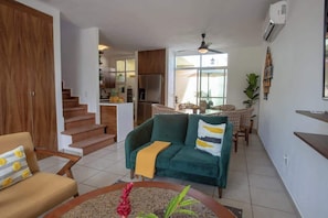 A living room with a sofa, a coffee table, and a dining area with a table and chairs. There is a staircase leading to an upper floor. - Riviera Nayarit Brand New House Close To The Beach (Bucerías)