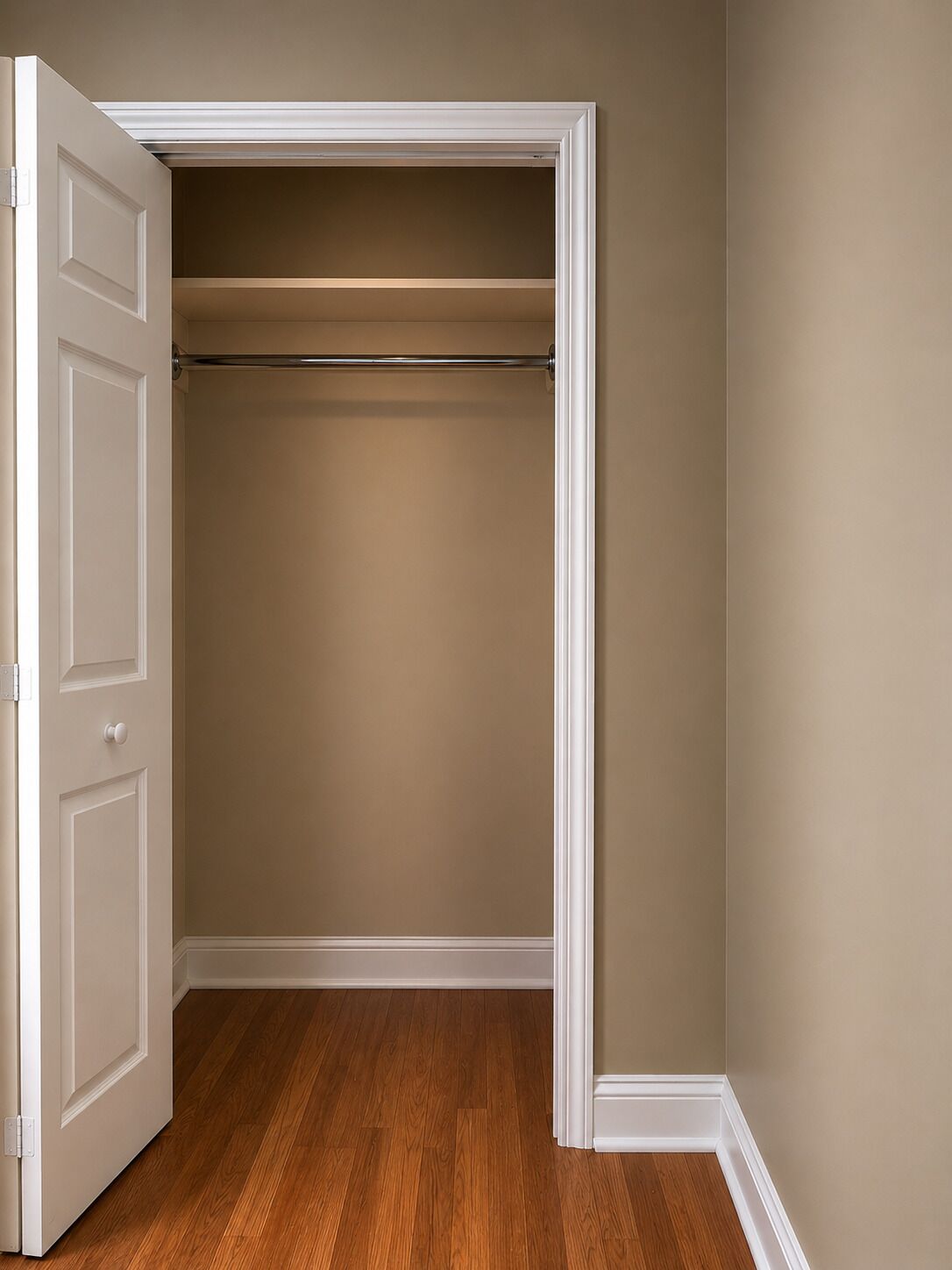 A walk-in closet with a wooden floor, white door, and beige walls.