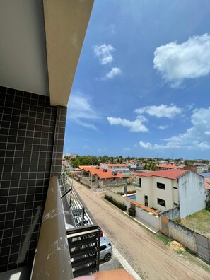 A balcony with a view of a residential area, a street, and a building with a red roof.