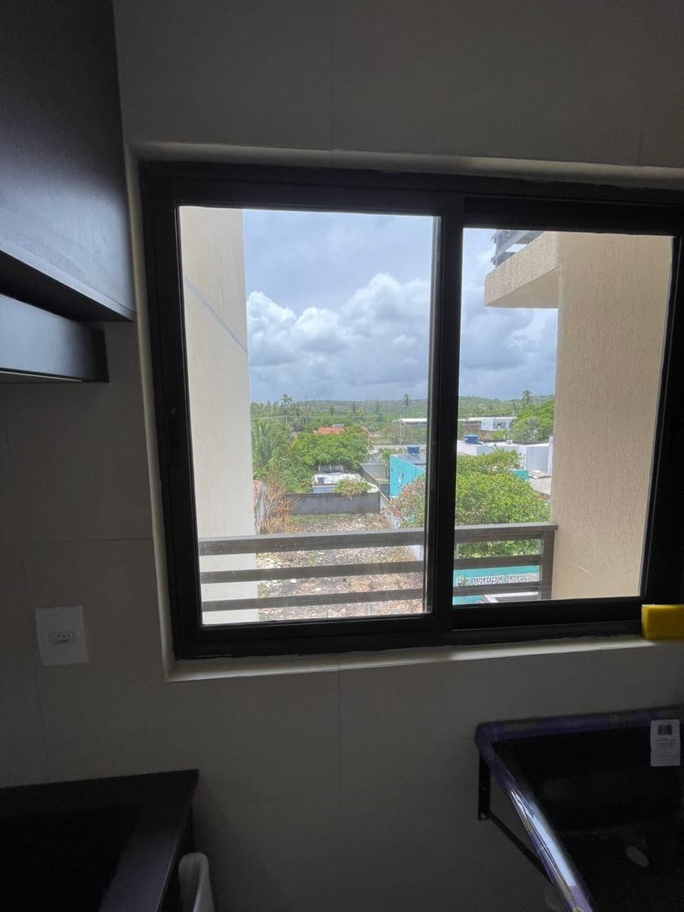 A room with a large window overlooking a residential area, a white wall, and a partial view of a kitchen counter.