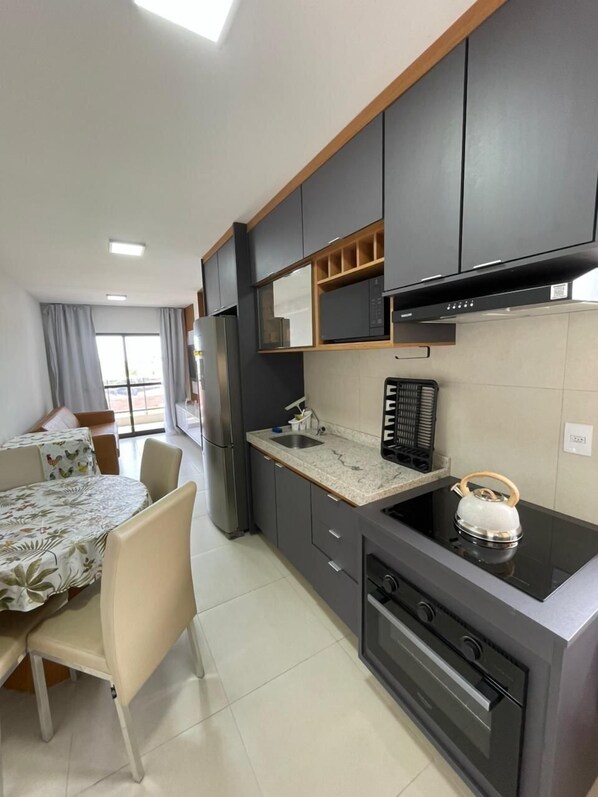 Une cuisine moderne avec des meubles de couleur sombre, un four à micro-ondes, une bouilloire et un coin repas comprenant une table et des chaises.