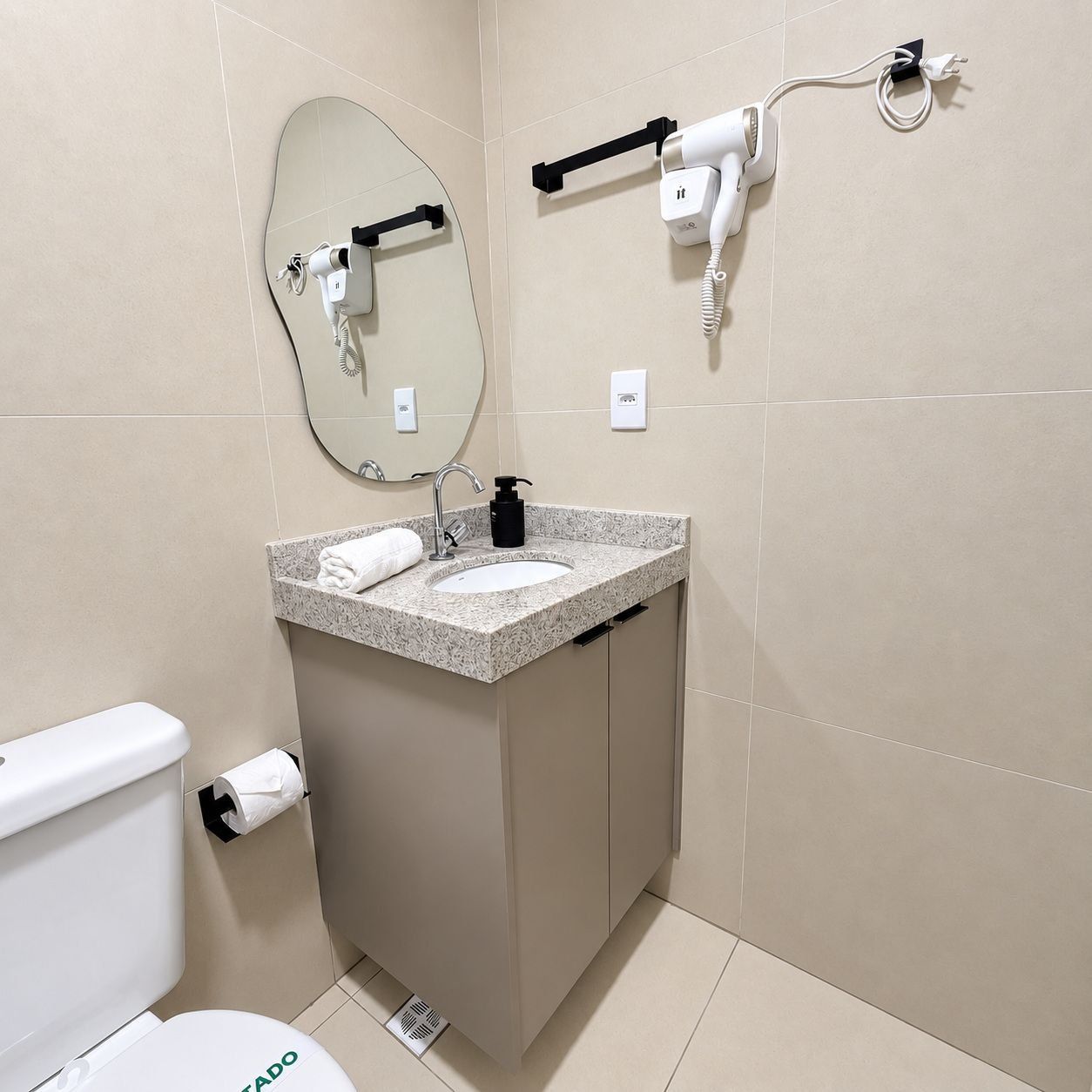 Et moderne badeværelse med toilet, vask, spejl, bøjle til håndklæder og hårtørrer.