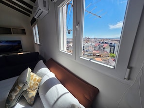A room with a bed, a window with a view of a cityscape, and an air conditioning unit. - eXperience Átic Valencia (València)