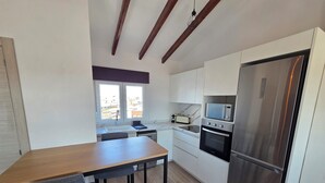 A modern kitchen with white cabinets, a stainless steel refrigerator, a built-in oven, and a window with a city view. - eXperience Átic Valencia (València)