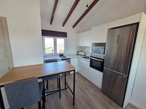 A modern kitchen with white cabinets, a stainless steel refrigerator, a built-in oven, and a window with a city view. - eXperience Átic Valencia (València)