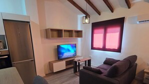 A modern living room with a wooden ceiling, a flat-screen TV, a sofa, a dining table, and a kitchen area. - eXperience Átic Valencia (València)