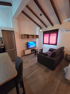 A modern living room with a wooden ceiling, a flat-screen TV, a sofa, a dining table, and a kitchen area. - eXperience Átic Valencia (València)