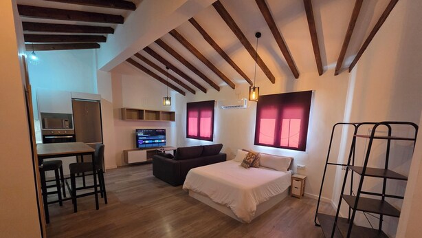 A compact room with a bed, a sofa, a TV, and a kitchenette. - eXperience Átic Valencia (València)