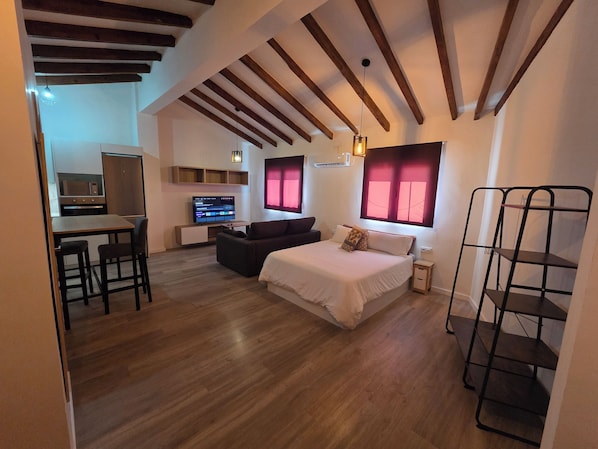 A compact room with a bed, a sofa, a TV, and a kitchenette. - eXperience Átic Valencia (València)