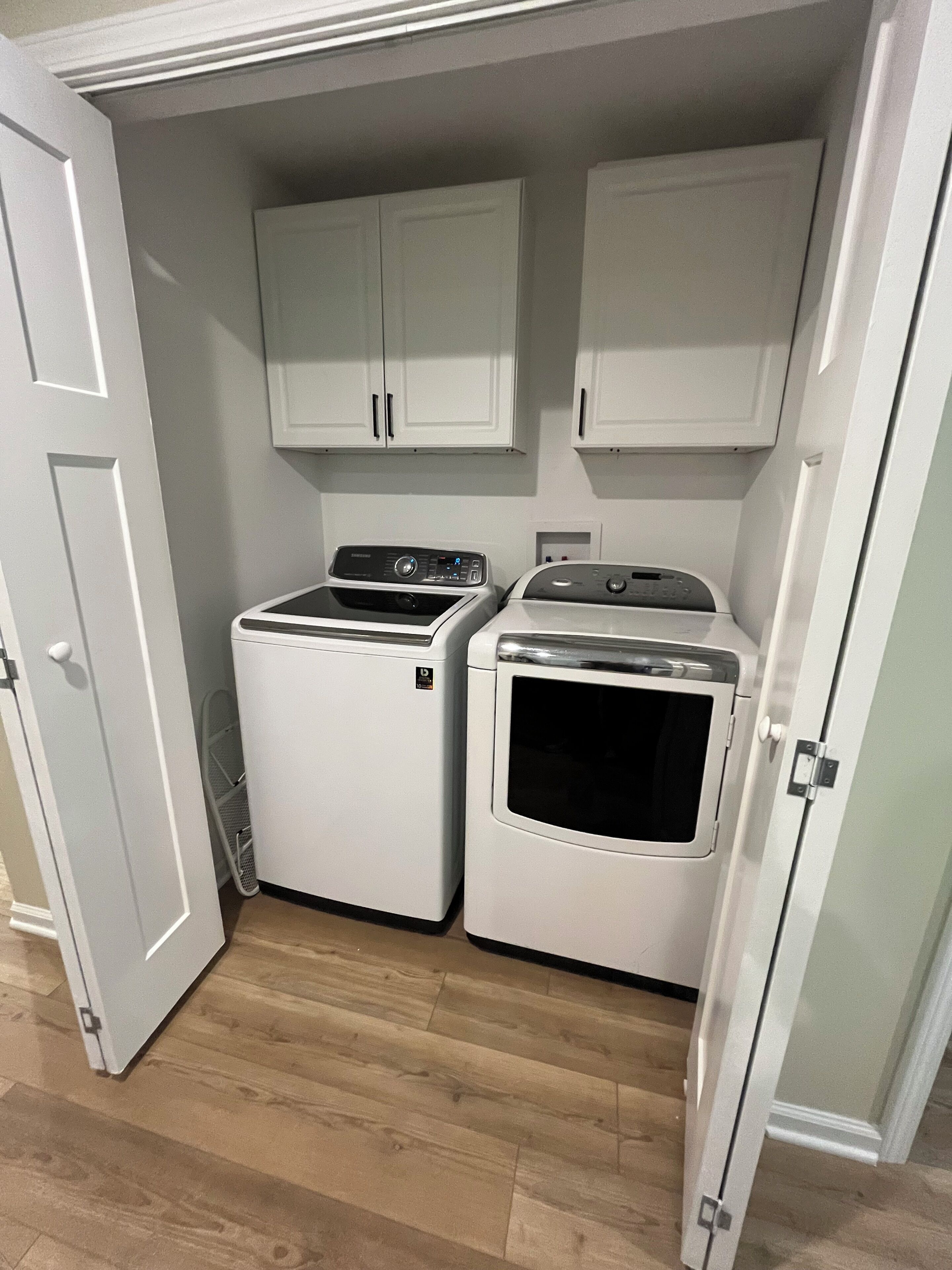 A laundry room with two white washing machines, a dryer, and white cabinets above.