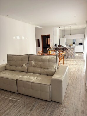A modern living room with a beige sofa, a dining area with wicker chairs, and a kitchen in the background. - COZY HOUSE COMPLETE IN ARRAIAL DAJUDA (PORTO SEGURO)