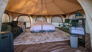Et teltinteriør med en seng, en sofa, et lille bord og en hylde med håndklæder.