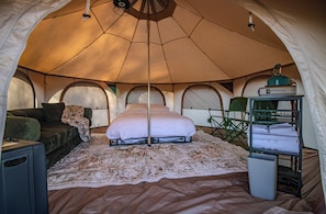 A tent interior with a bed, a sofa, a small table, and a shelf with towels. - JOURNEY SOUTHWEST RESORT (Farmington)