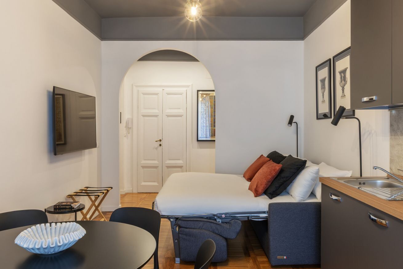 Ein kleines Zimmer mit Bett, einer Küchenzeile, einem Esstisch und einem Fernseher.