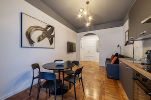 A modern kitchen with a dining area, a large abstract painting, and a staircase leading to another level.
