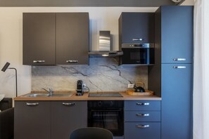 A compact kitchen with dark cabinets, a built-in oven, a microwave, and a coffee machine.