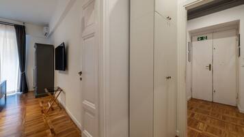 A hallway with wooden flooring, white doors, a flat-screen TV mounted on the wall, and a staircase leading to a door marked with an emergency exit sign.