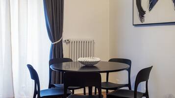 Zona pranzo con tavolo rotondo, quattro sedie, una ciotola bianca, un termosifone e un quadro appeso al muro.