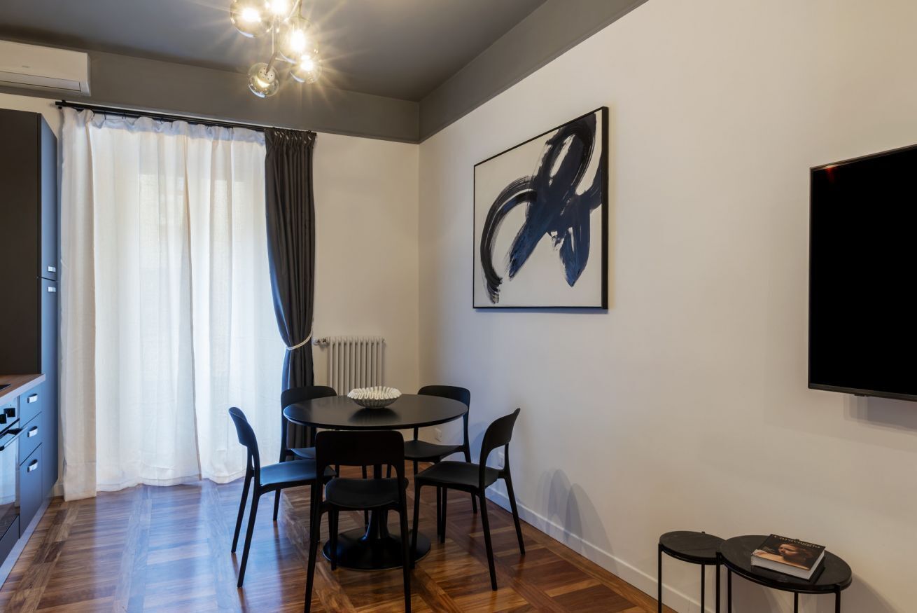 A modern dining area with a round table, black chairs, a black TV, and a large abstract painting on the wall.