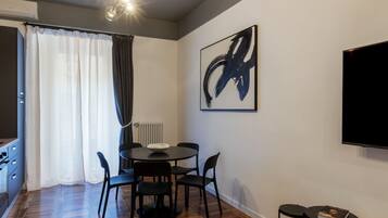 A modern dining area with a round table, black chairs, a black TV, and a large abstract painting on the wall.