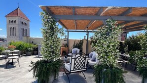 Eine Terrasse im Freien mit Sitzgelegenheiten, einer Pergola und einem Turm im Hintergrund.