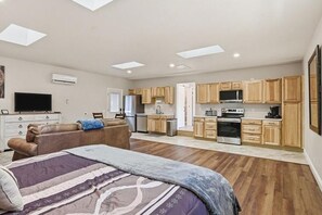 A spacious room with a bed, a sofa, a kitchen area with wooden cabinets, and a television. - Ranch Studio Retreat with Mountain Views, Longmont, Colorado (Longmont)
