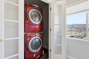 A laundry room with two stacked front-loading washing machines, a window with a view of a fenced area and hills, and a white door. - Ranch Studio Retreat with Mountain Views, Longmont, Colorado (Longmont)