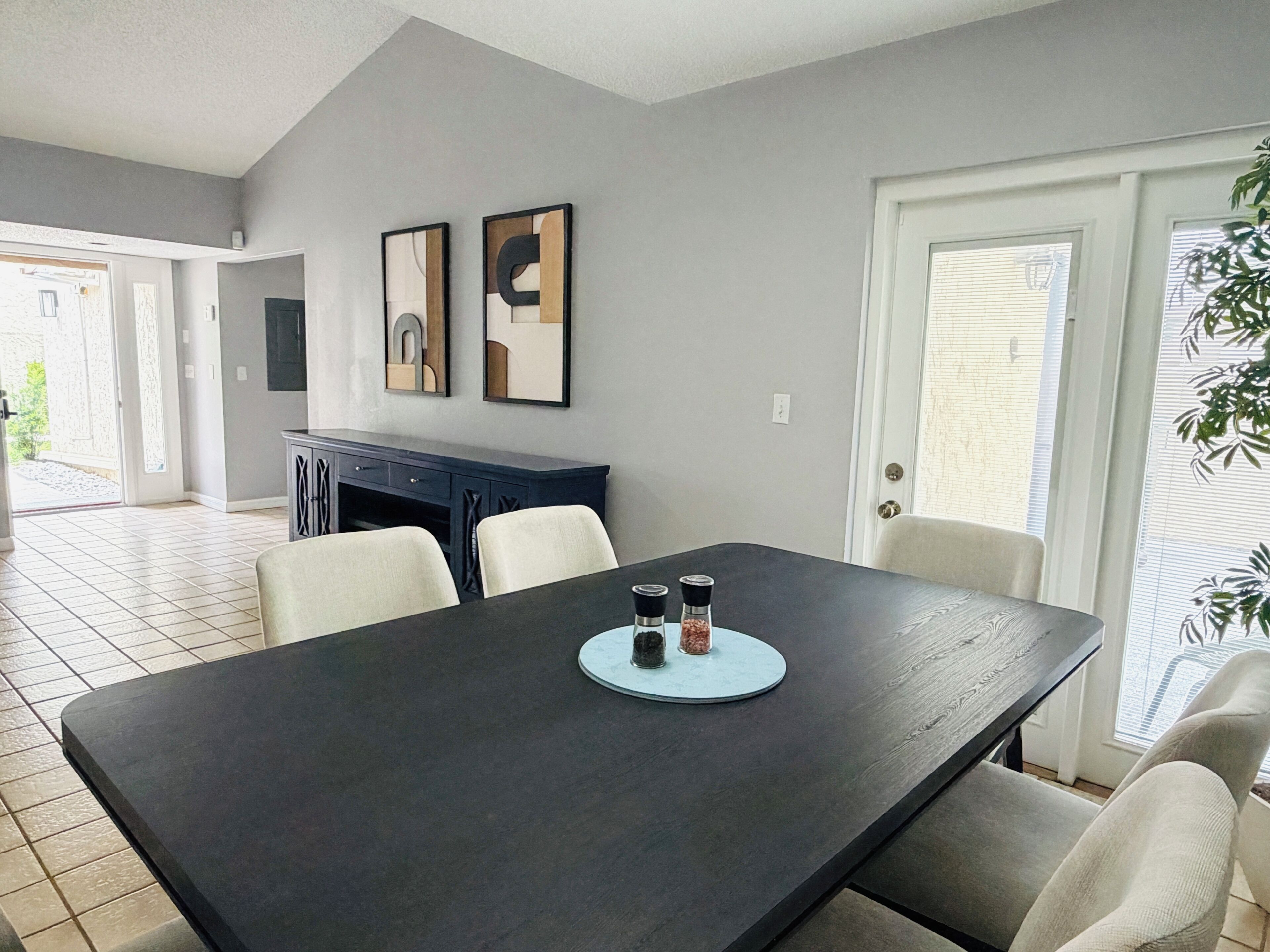 A dining area with a dark wooden table, two framed artworks on the wall, and a door leading outside.
