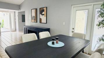 A dining area with a dark wooden table, two framed artworks on the wall, and a door leading outside.