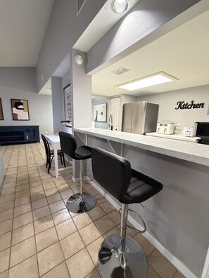 A modern kitchen with a bar area, a dining table with chairs, and a tiled floor.