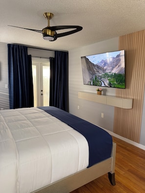 Une chambre à coucher avec un lit, un ventilateur de plafond, un téléviseur fixé au mur et un mur recouvert de panneaux de bois.