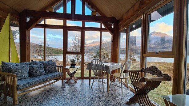 Una stanza con soffitto in legno, ampie finestre, un divano, un tavolo e sedie.