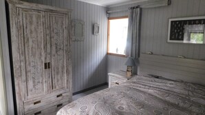Una camera da letto con un ampio armadio, un comodino con una lampada, una coperta a fantasia e una finestra con tende.