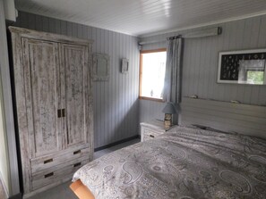 Ein Schlafzimmer mit einem Bett, einem Kleiderschrank, einem Nachttisch, einer Lampe, einem Fenster und einem Spiegel.