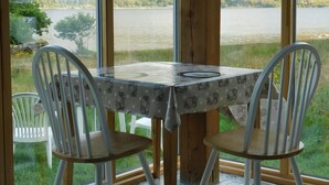 Zona pranzo con tavolo e sedie, ampie finestre vista su un lago e delle colline.