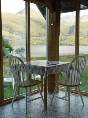 Un comedor con una mesa y sillas, ventanas amplias con vista a un lago y colinas.