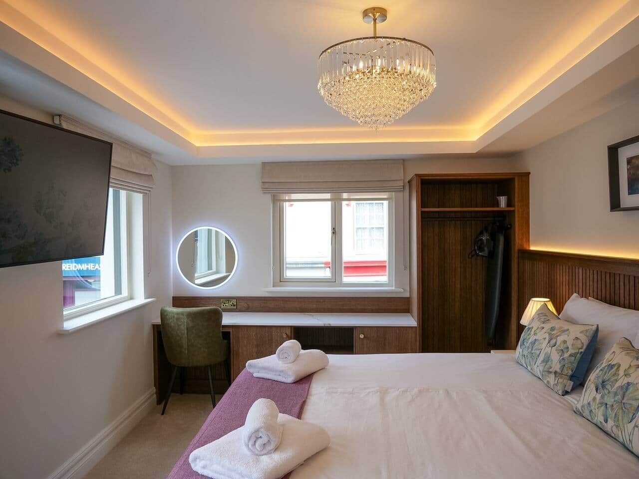 Een hotelkamer met een bed, nachtkastje, stoel, bureau en een groot raam.