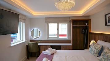 Een hotelkamer met een bed, nachtkastje, stoel, bureau en een groot raam.