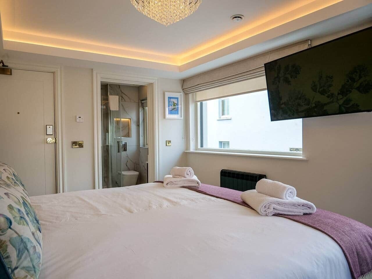 Een slaapkamer met een bed, een raam, een deur en een douchehoek.