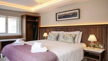 Habitación de hotel con una cama grande, dos mesitas de noche, un candelabro, una ventana y un cuadro en la pared.