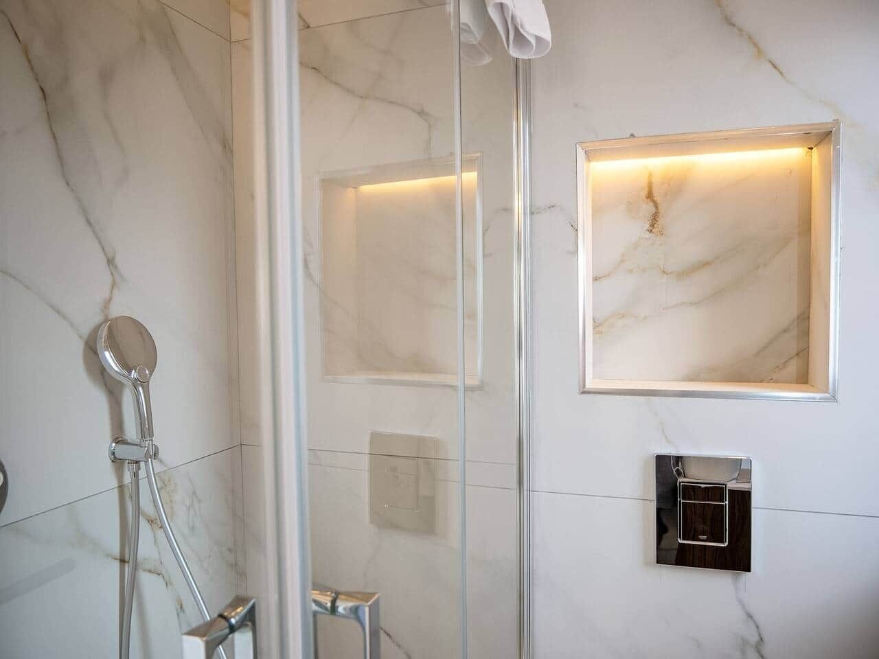 A modern bathroom with a glass-enclosed shower, a handheld showerhead, and a wall-mounted light fixture.