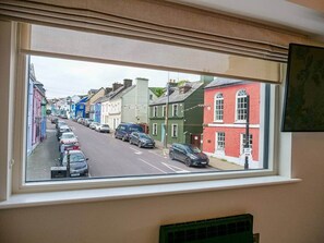 Ein Fenster mit Blick auf eine Straße, gesäumt von bunten Häusern und parkenden Autos.