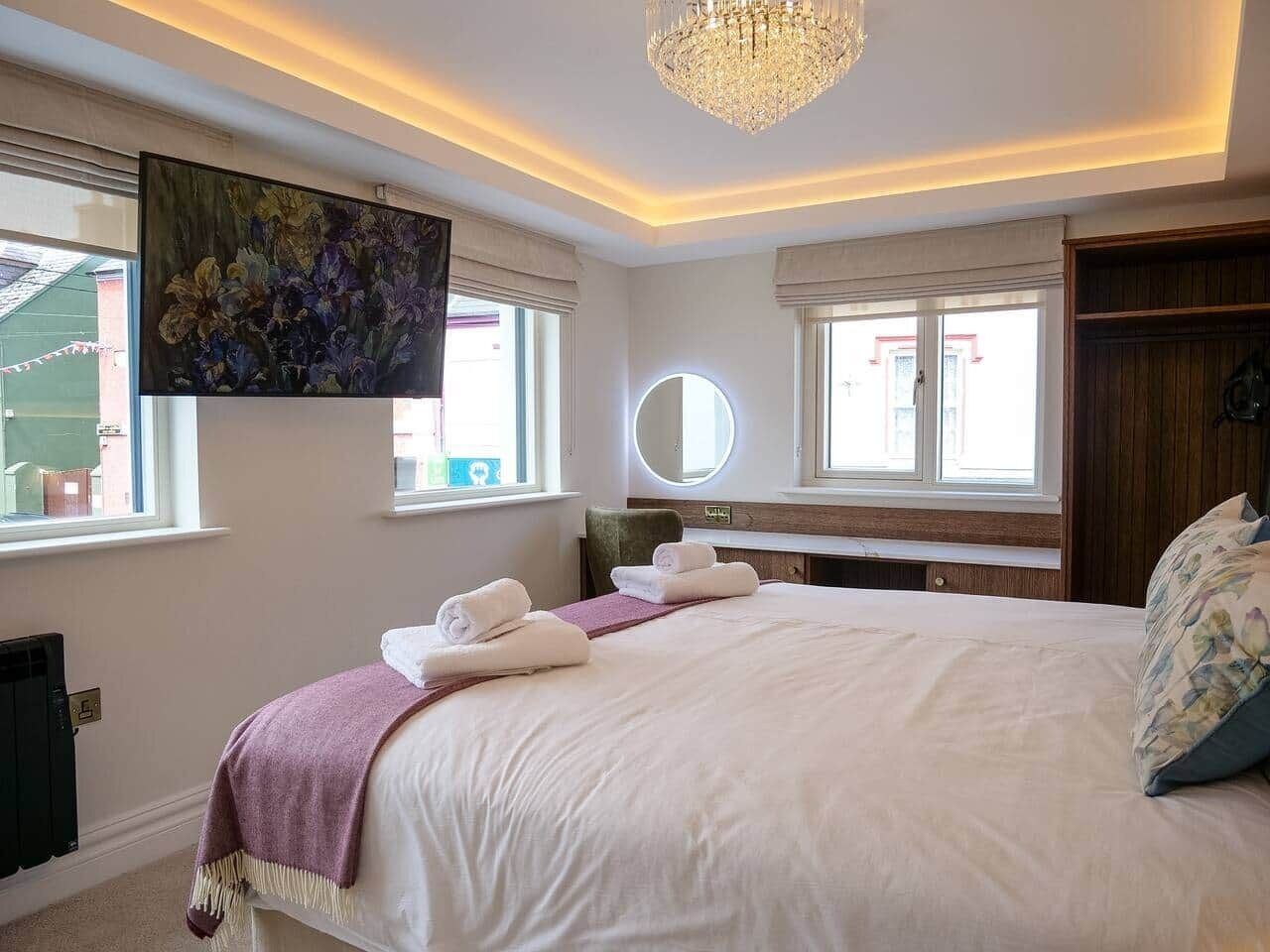 Une chambre d’hôtel avec un grand lit, un miroir rond et un lustre.
