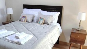 Ein ordentlich bezogenes Bett mit Kissen und Decke, ein Nachttisch mit Lampe und ein kleiner Teppich auf dem Boden.