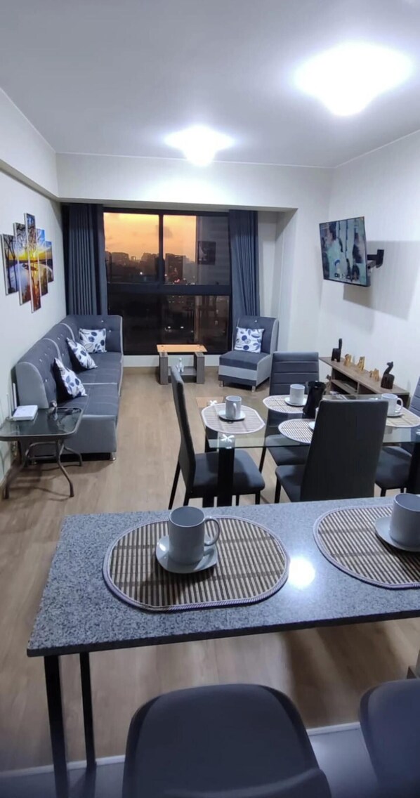 Ein modernes Wohnzimmer mit einer Couch, einem Esstisch, Stühlen und einem an der Wand montierten Fernseher.
