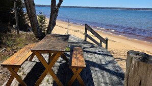 Eine Holzterrasse mit Picknicktischen und einem Holzzaun mit Blick auf einen Strand und das Wasser.