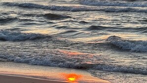 Ein Strand mit Wellen, einem Sonnenuntergang und einer fernen Küstenlinie.