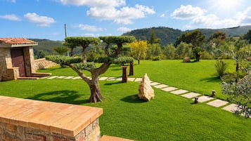 Ein gepflegter Garten mit einer Steinmauer, einer hölzernen Bank und freiem Blick auf die umliegende Landschaft.